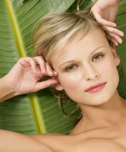 Headshot of woman with short blonde hair laying against a large leaf