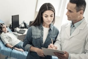 Skillful nice male doctor standing near his patients mother and taking notes