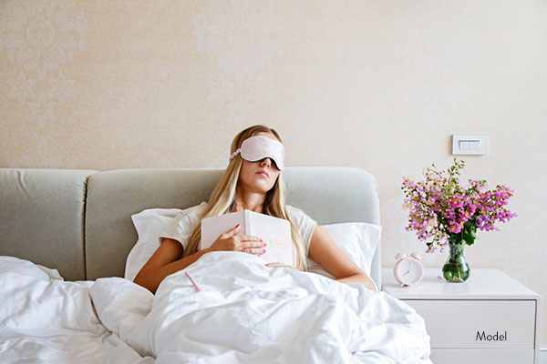 Woman sleeping upright with an eye mask on and a book in her hand