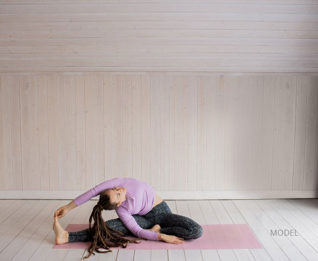 Woman in a purple shirt and grey leggings doing a stretching exercise