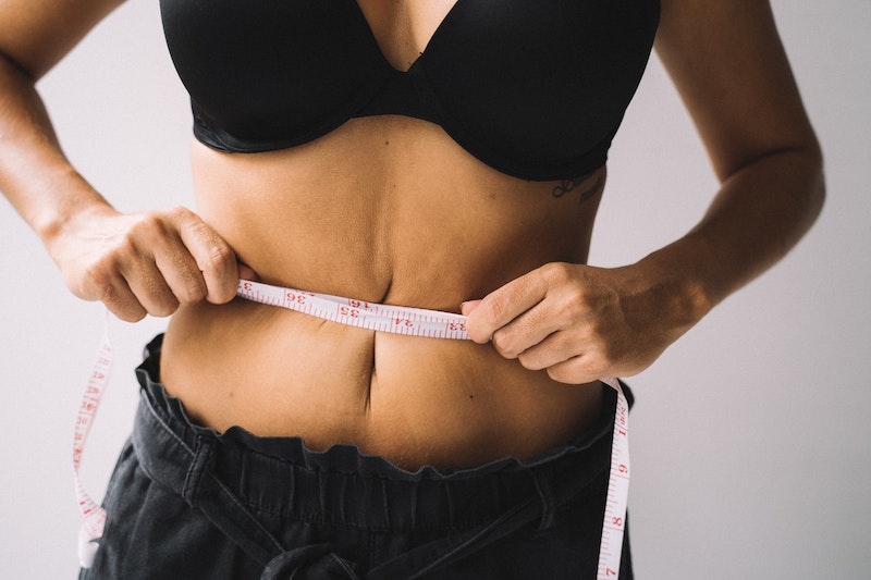 A woman in a black bra and black pants holding the measuring tape