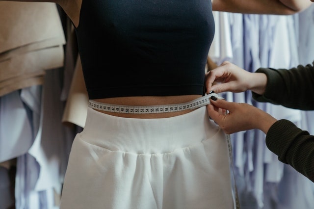 a woman measuring the waist of another woman after a tummy tuck