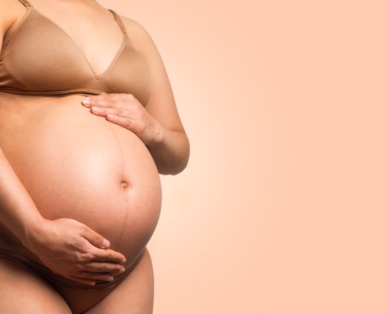 Close-up image of a pregnant belly against a peach background.