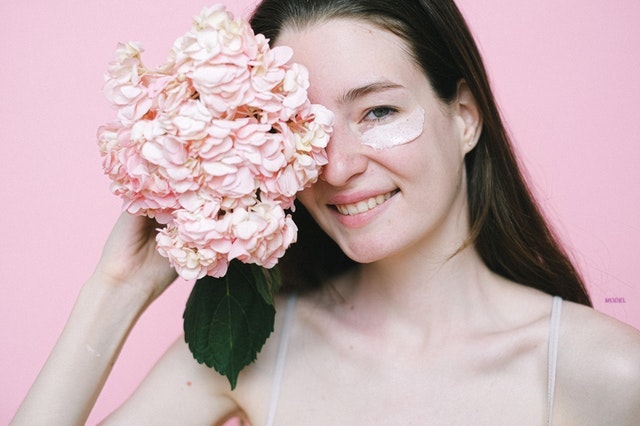 A smiling woman holding flowers with skin cream under her eyes.