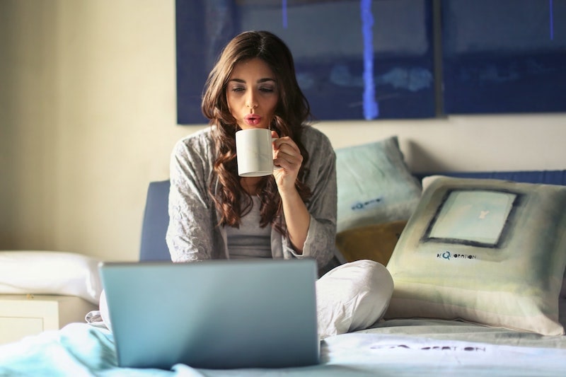 A woman drinking coffee while searching on her laptop