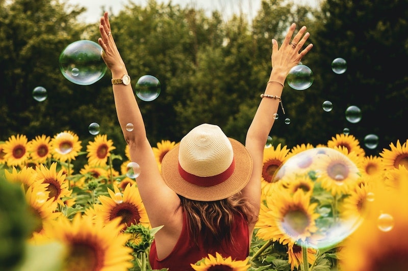 A girl spending time in nature with arms stretched up in sunflower field