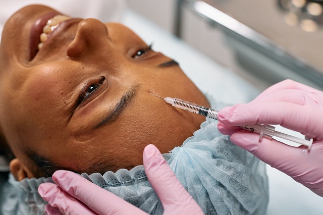 A person with pink gloves injecting Botox into a woman's forehead