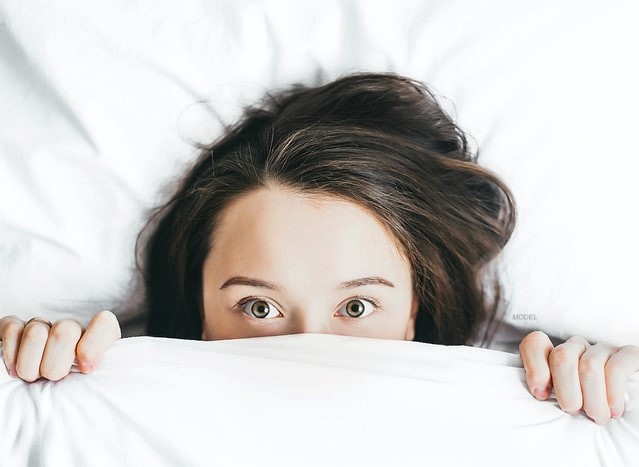 Woman hiding under a quilt.