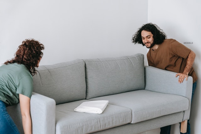 A man and a woman moving a large gray sofa