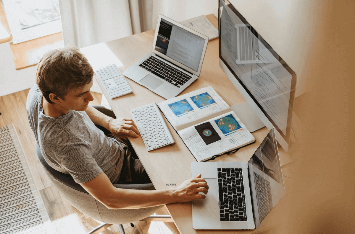 A man using three computers in his home office.