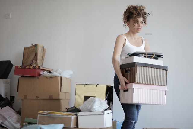 Woman carrying three boxes and moving away from a pile of things