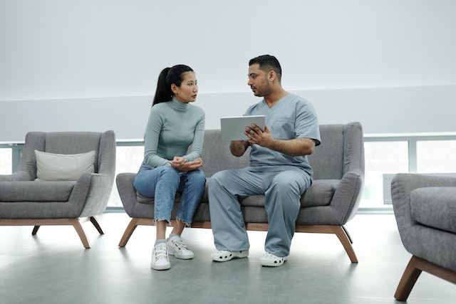 Woman sitting on a couch in a hospital waiting room and talking to a surgeon in scrubs