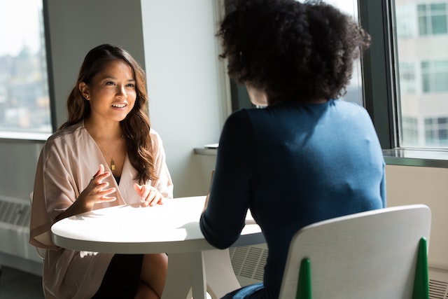 Two women sitting at a table and talking about ways to combat the stigma around plastic surgery