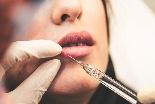 Person injecting a lip filler into a woman's lips