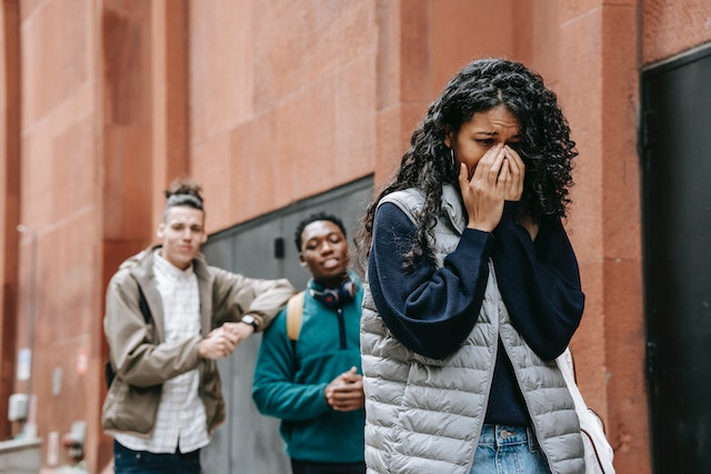 Two men gossiping about a woman that's walking down the street and holding her hands over her face