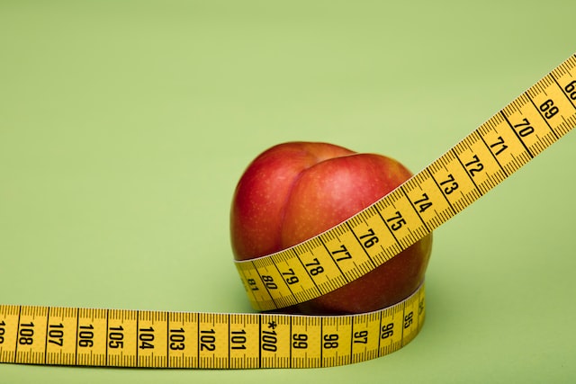 A tape measurer around a peach on a green surface.