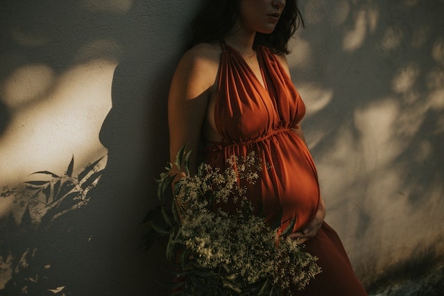 A picture of a pregnant woman in the third-trimester holding flowers in an orange dress.

