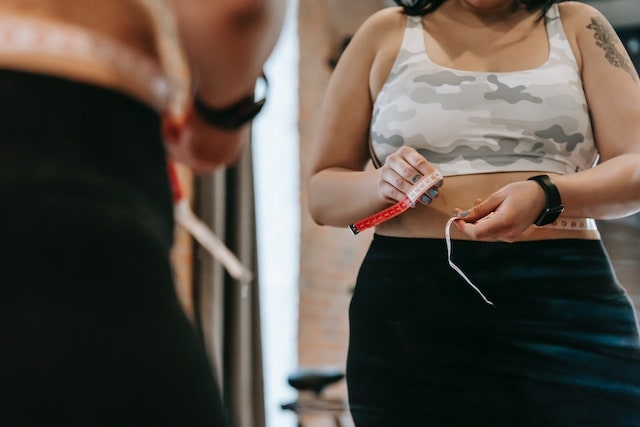 A woman measuring her abdominal area in the gym.