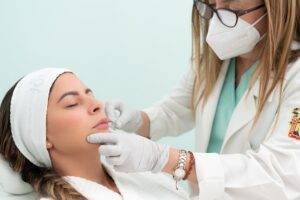 A masked doctor injects a lip filler into a patient.