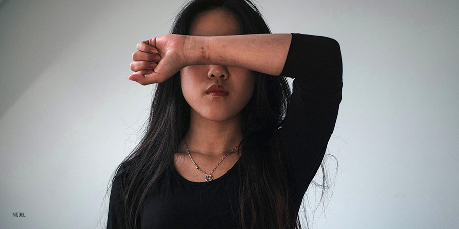 A young woman hiding her face from substance abuse and body image pressure in California