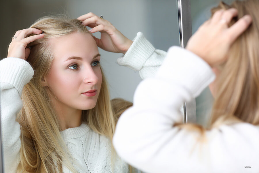 Woman looking in the mirror for flaws in her appearance.